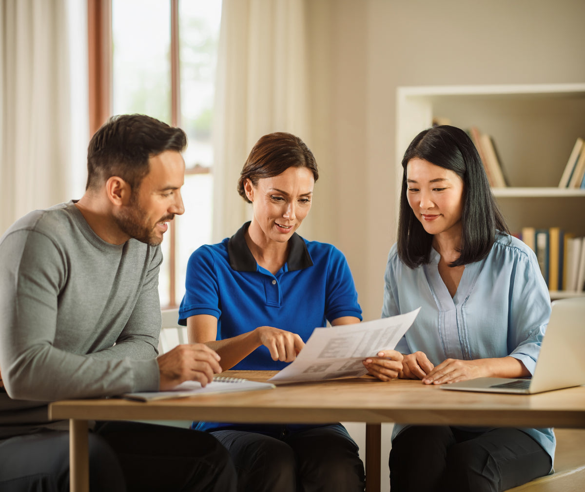Three people sitting around a table reviewing documents together.